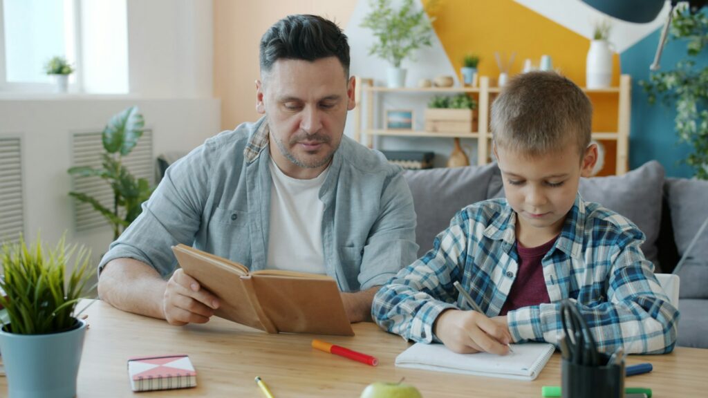 Father reading while his son does homework, parenting a child with ADHD