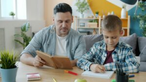 Father reading while his son does homework, parenting a child with ADHD